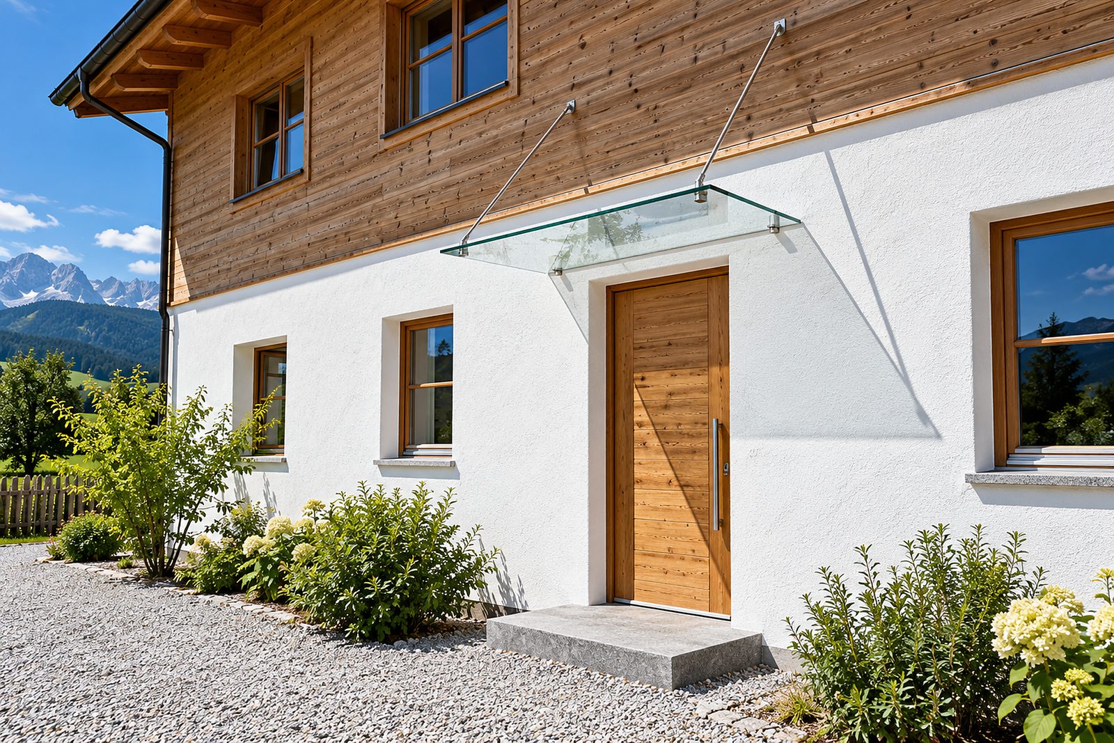 Ein Glasvordach aus klarem Sicherheitsglas an zwei Edelstahlstangen über der Holztür eines oberbayerischen Hauses, harte Mittagssonne